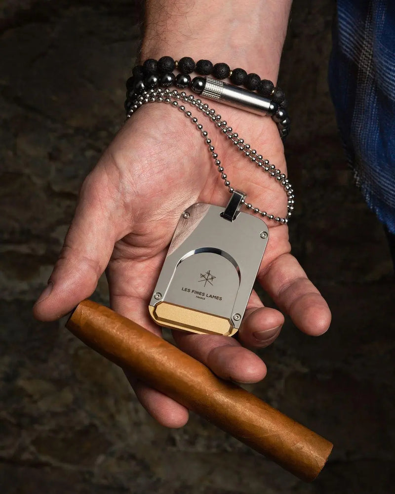 Hand holding a cigar and a Les Fines Lames Le TAG T135 as part of a cigar travel kit