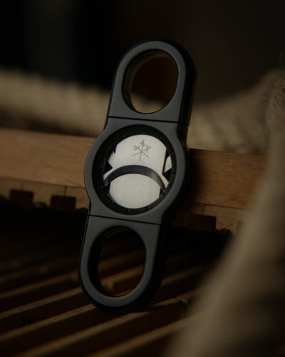 La Guillotine Rotor by LES FINES LAMES, a black stainless steel guillotine cigar cutter displayed on a wooden surface