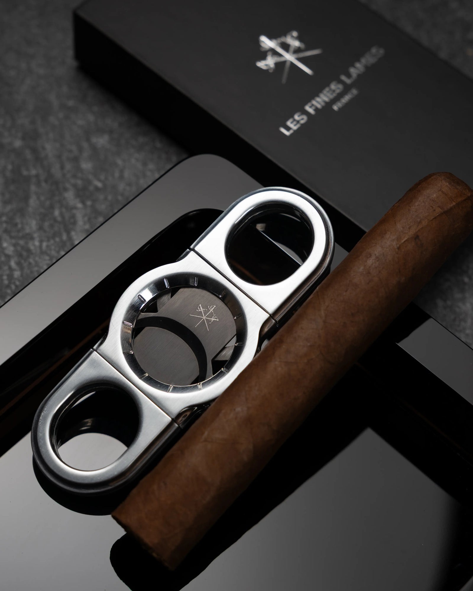 La Guillotine - ROTOR Chrome by LES FINES LAMES, chrome cigar cutter displayed with a cigar on obsidian ashtray