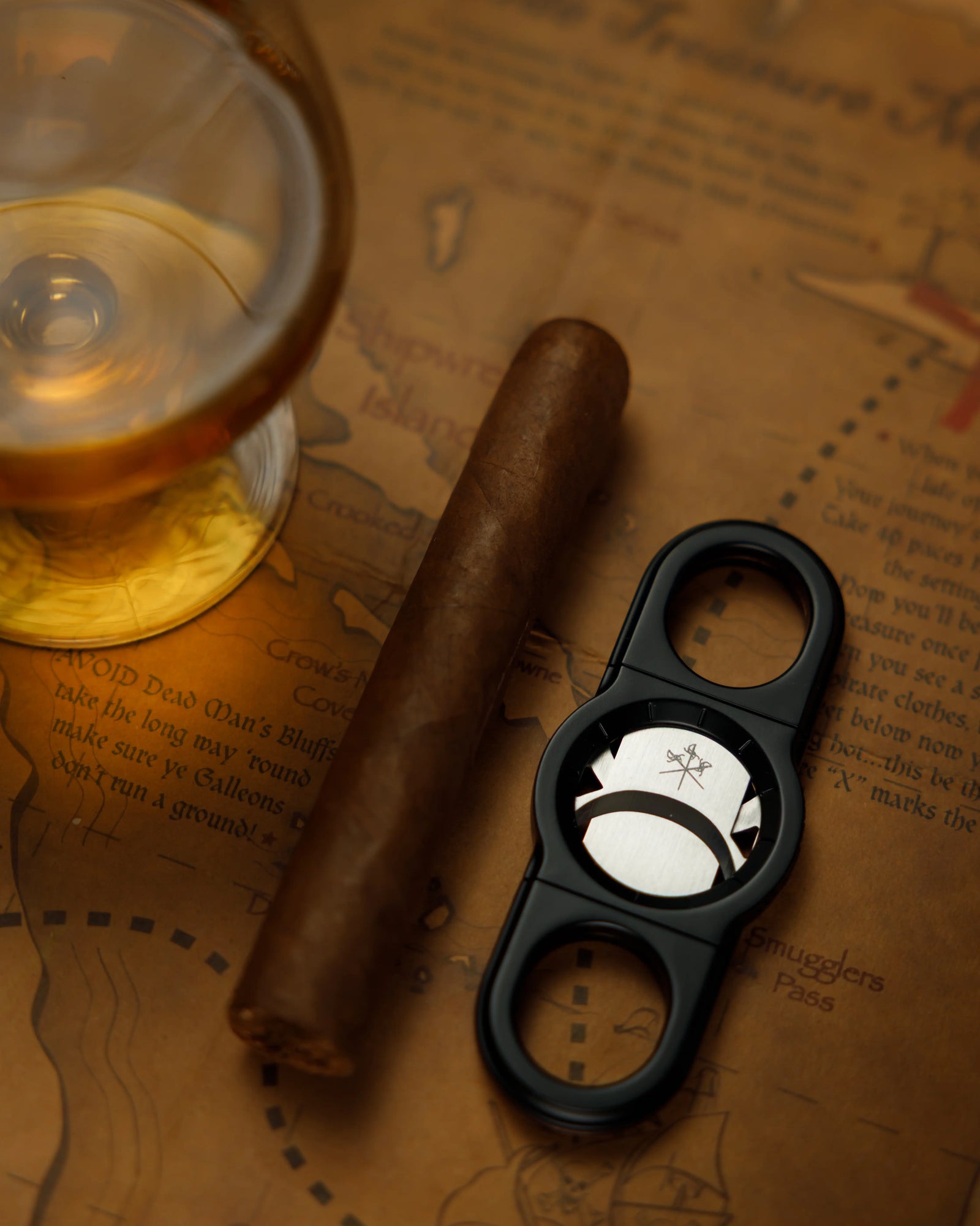 La Guillotine - ROTOR Black by LES FINES LAMES, black cigar cutter displayed with a cigar and a glass on a vintage map
