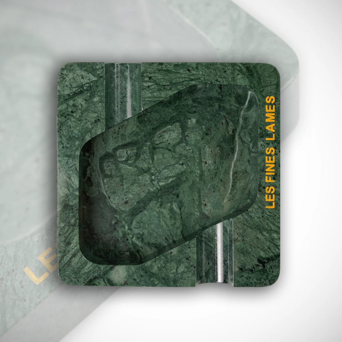 A square green marble-patterned coaster with rounded corners, featuring a central dark green stone motif and text reading 'LES FINES LAMES' on the right edge, shown on a light gray background.