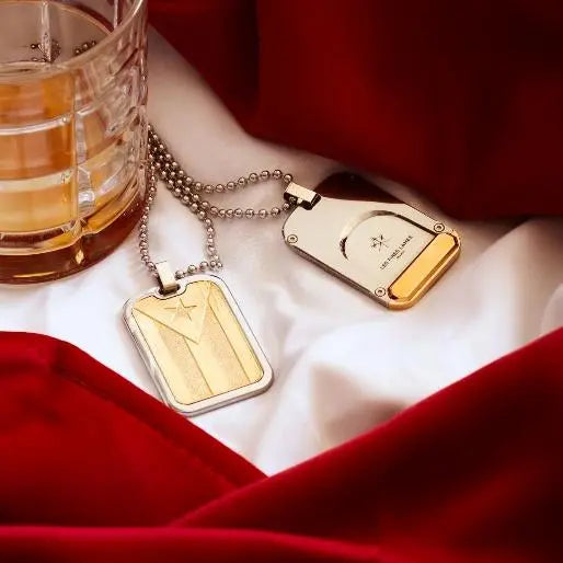 Le TAG T100 Flag Cuba Gold cigar accessory displayed on red fabric next to a glass