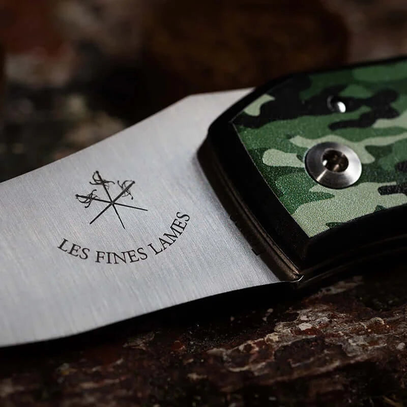 Close-up of Le PETIT Camo Woodland knife with green camouflage handle on a dark surface